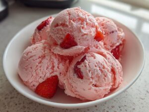Close-up of several scoops of pink strawberry ice cream garnished with fresh strawberry pieces in a white bowl.