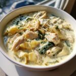 Close-up of a bowl of creamy white chicken lasagna soup with chunks of chicken, spinach, and noodles.