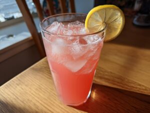 A tall glass filled with ice and bright pink lemonade, garnished with a fresh lemon slice.
