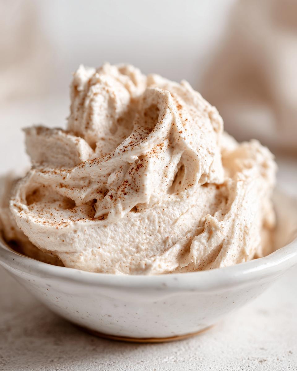 Close-up of fluffy, whipped cinnamon butter sprinkled with extra cinnamon in a small white bowl.