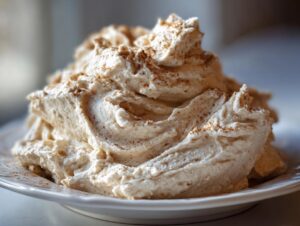 A close-up of a generous swirl of fluffy, light brown cinnamon butter sprinkled with ground cinnamon.