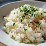 Close-up of fluffy garlic butter rice served in a white bowl and garnished generously with fresh chopped parsley.