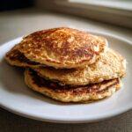 A stack of four fluffy oatmeal pancakes with golden-brown, slightly crispy edges on a white plate.