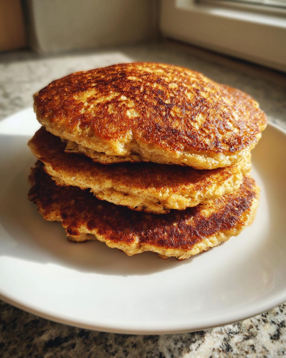 A stack of three golden-brown, fluffy oatmeal pancakes resting on a white plate.