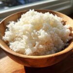 Close-up of fluffy, perfectly cooked sushi rice piled high in a small wooden bowl, ready for rolling.