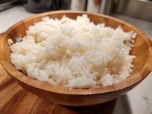 Close-up of perfectly fluffy, white sushi rice steaming slightly in a round wooden bowl.