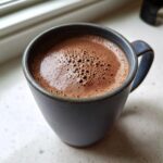 Close-up of rich, frothy mexican hot chocolate served in a dark blue ceramic mug.