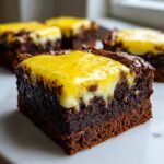 Close-up of a fudgy chocolate brownie topped with a thick layer of bright yellow lemon topping.