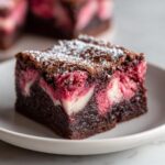 A close-up of a fudgy strawberry brownies square topped with powdered sugar, showing pink fruit swirls.