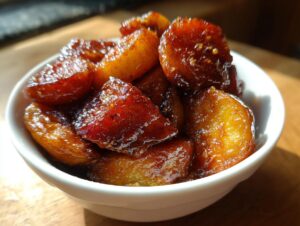 Close-up of caramelized, glistening chunks of baked apple served in a small white bowl.