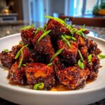 Close-up of crispy, glazed honey garlic chicken pieces piled high and garnished with fresh green onions.
