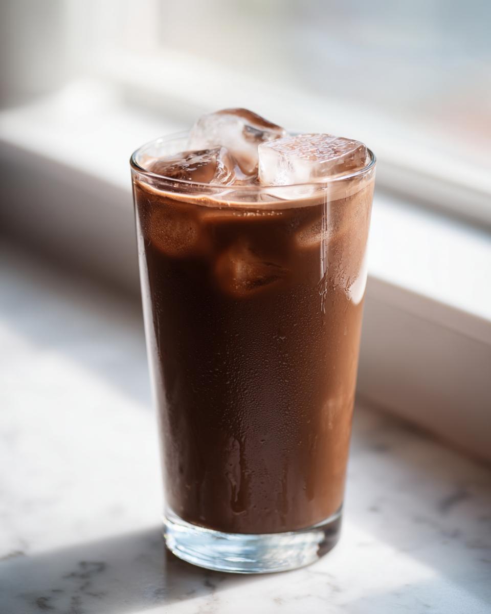 A tall glass filled with refreshing iced chocolate milk and large ice cubes, glistening in natural light.