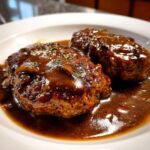 Close-up of two juicy Salisbury steak patties covered in thick, rich brown mushroom gravy.