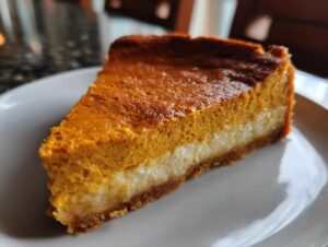 A close-up of a perfect slice of keto pumpkin cheesecake showing distinct pumpkin and cream cheese layers.