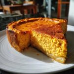 A close-up of a rich, orange keto pumpkin cheesecake with a slice removed, sitting on a white plate.