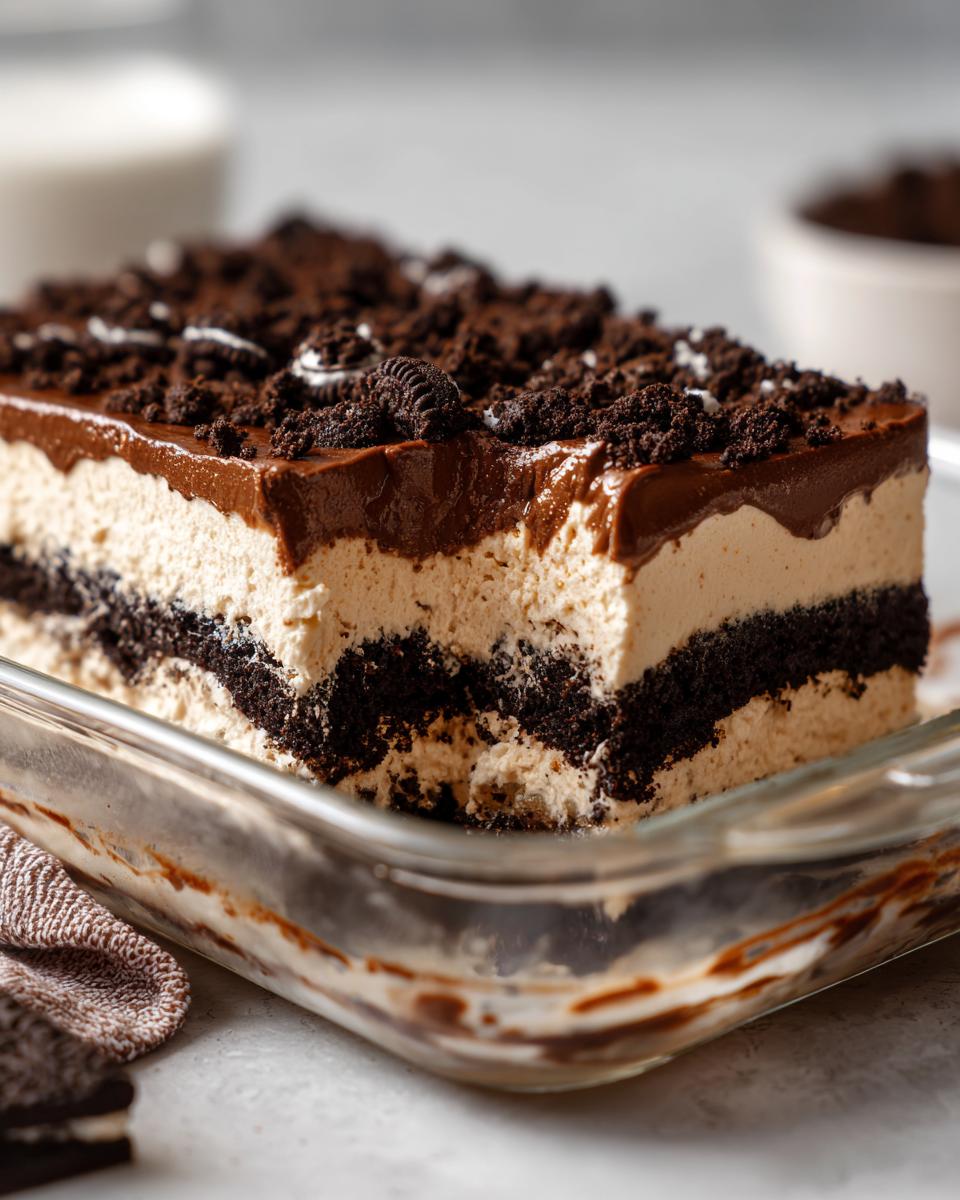 A close-up view of a layered slice of dirt cake in a glass dish, featuring chocolate cookie crumbs and creamy filling.