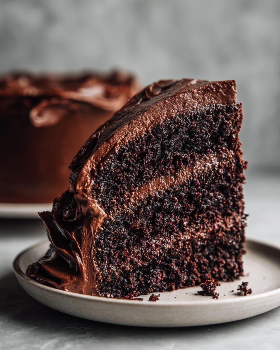 Close-up of a rich, dark slice of chocolate fudge cake showing the moist crumb and thick frosting.