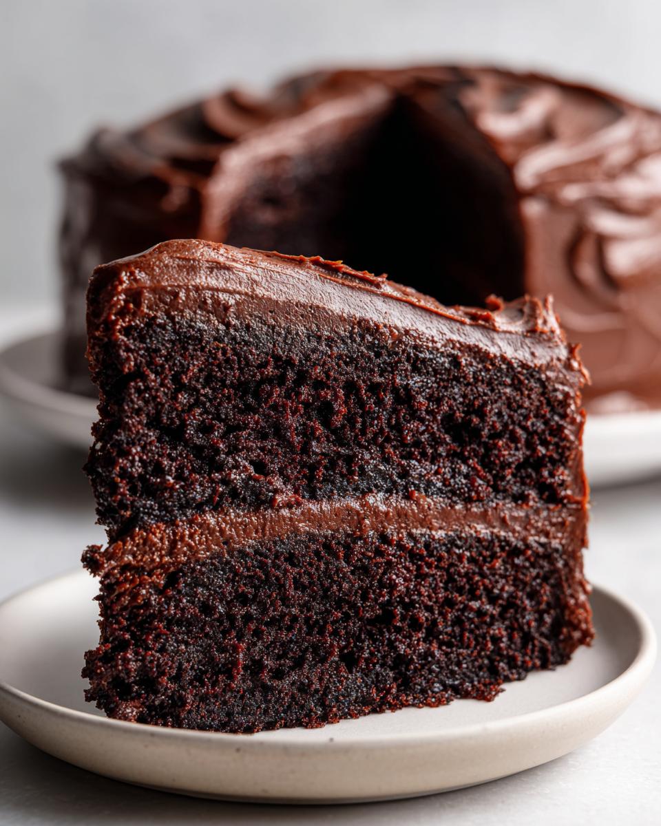 Close-up of a moist slice of dark chocolate fudge cake with thick chocolate frosting layers.