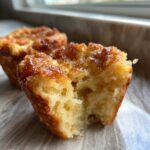 A close-up shot of a french toast muffin broken open, showing its soft, airy interior and caramelized, sugary top.