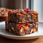 Two stacked, moist slices of rich fruit cake recipe loaded with candied cherries and nuts.