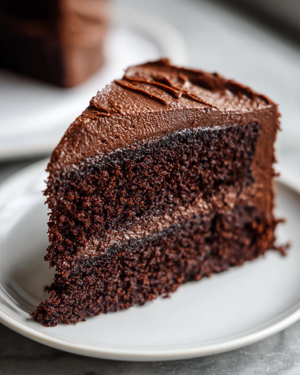 Close-up of a moist slice of homemade chocolate cake layered with rich chocolate frosting.