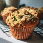 Close-up of a moist pistachio muffins with a golden brown crumb topping resting on a cooling rack.