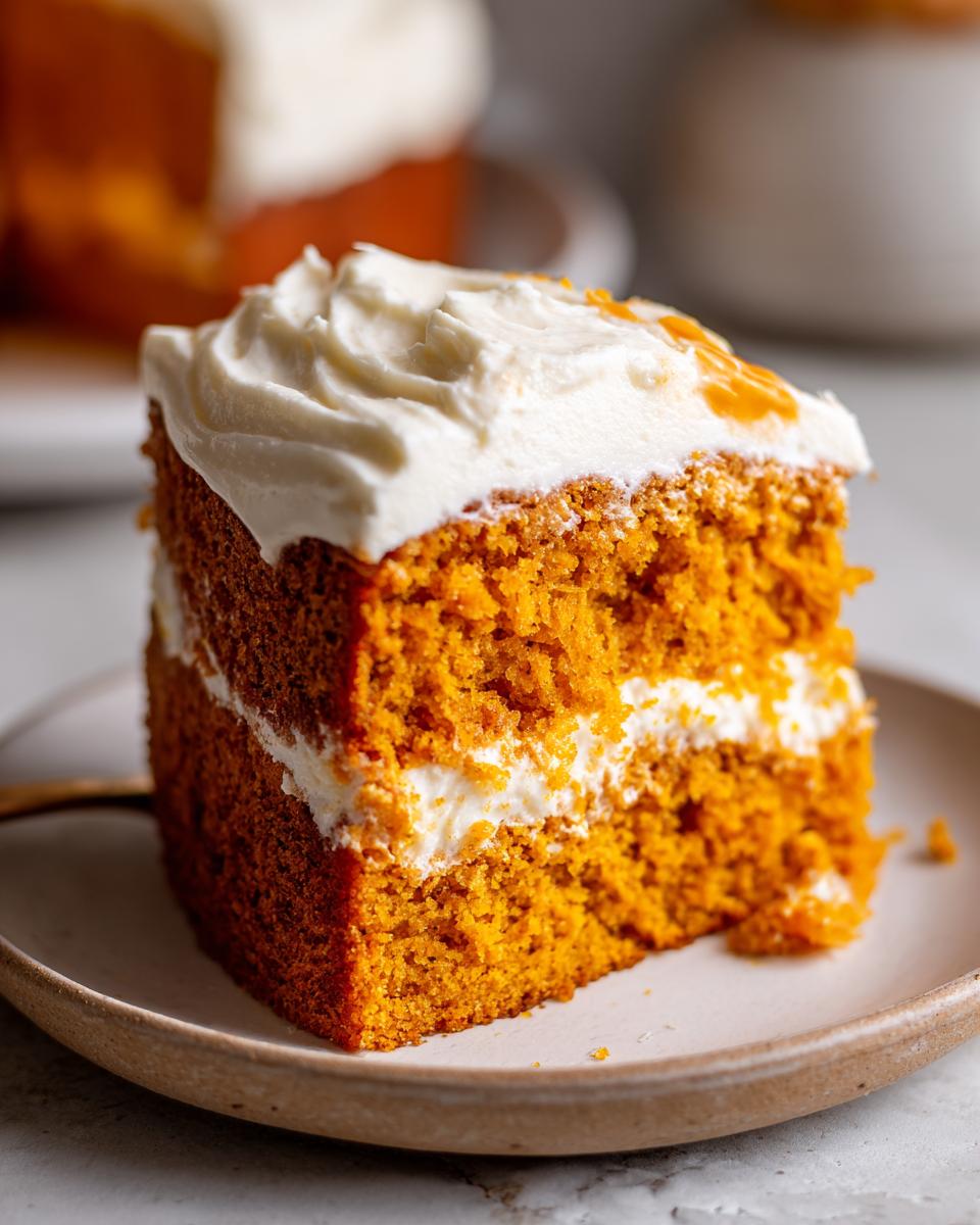 Close-up of a moist slice of orange pumpkin poke cake layered with white frosting.