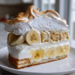 A tall, layered slice of old-fashioned banana pudding featuring vanilla wafers, fresh banana slices, and toasted meringue topping.