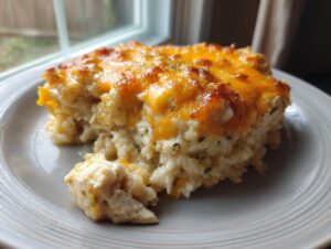 A close-up of a square serving of creamy chicken and rice casserole topped with melted cheddar cheese.