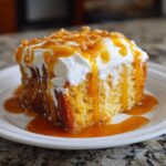 A moist slice of pumpkin poke cake topped with whipped cream, caramel drizzle, and chopped nuts.