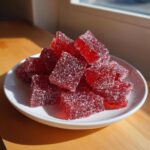 A pile of glistening, sugar-coated, ruby-red squares resembling cinnamon rock candy on a small white plate.