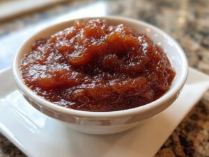 Close-up of thick, dark brown homemade apple butter served in a small white bowl.