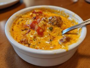 Close-up of a small white bowl filled with bubbling, cheesy Sausage rotel dip featuring sausage chunks and diced tomatoes.