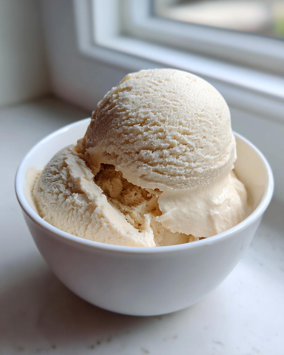 Two scoops of creamy vanilla protein ice cream served in a small white bowl near a window.