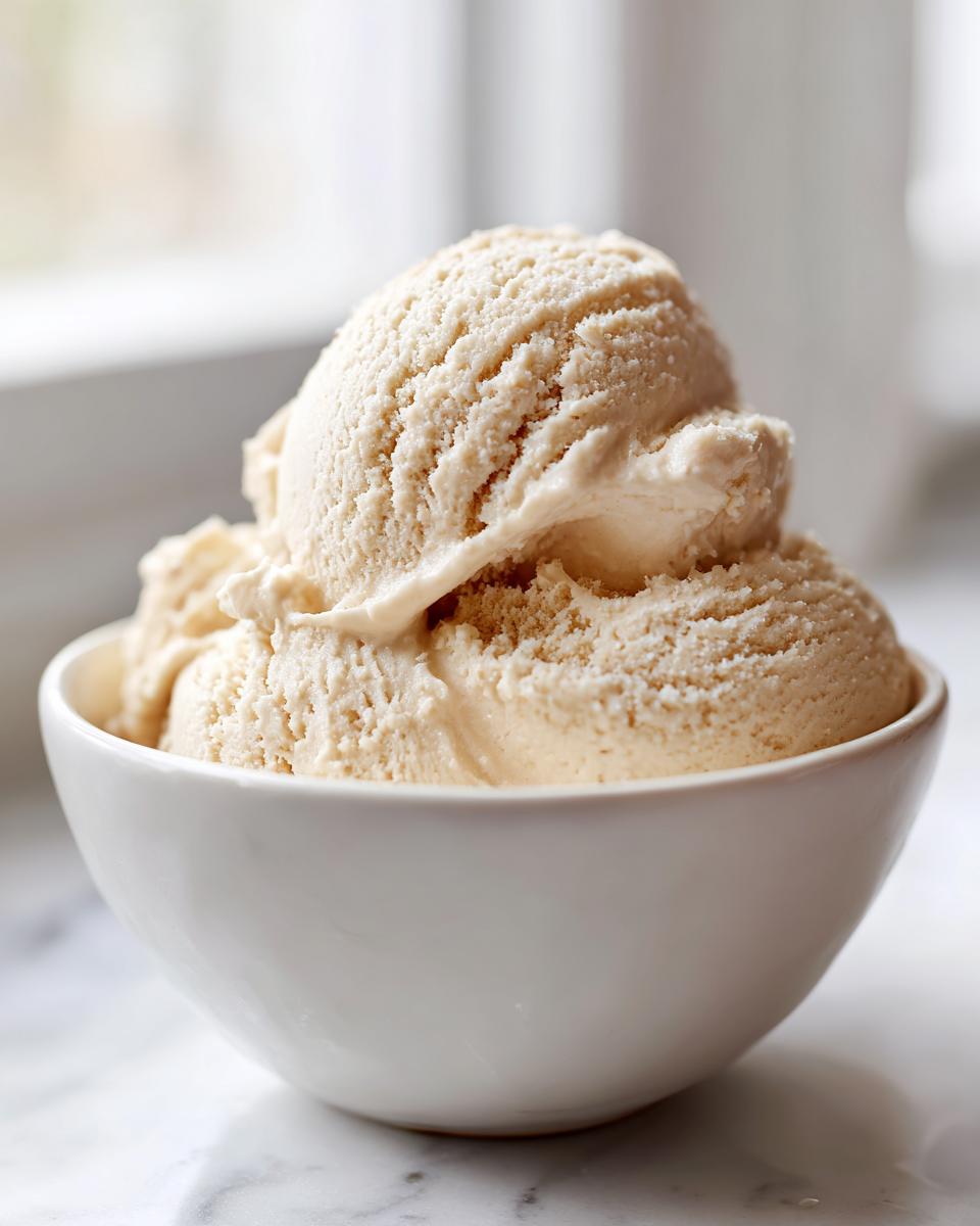 Close-up of several scoops of light brown protein ice cream served in a white bowl.