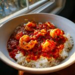 A white bowl filled with white rice topped generously with rich, red sauce and plump shrimp in this delicious shrimp creole.