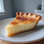 A close-up of a slice of creamy buttermilk pie with a beautifully browned, caramelized top crust.