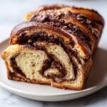 A close-up shot showing a slice cut from a freshly baked chocolate babka, revealing rich chocolate swirls inside the sweet bread.