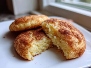 Close-up of a soft, light-colored snickerdoodle cookie broken in half, showing its texture, dusted with cinnamon sugar.