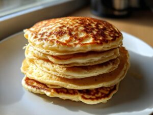 A tall stack of five fluffy sourdough discard pancakes with golden-brown, lacy tops on a white plate.