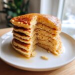 Close-up of a tall stack of fluffy sourdough discard pancakes drizzled with syrup.