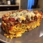 A thick slice of baked spaghetti pie showing layers of pasta, meat sauce, and melted cheese topping.