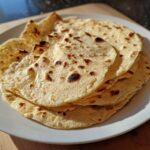 A stack of freshly made, lightly charred corn tortillas resting on a white plate.