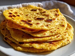 A stack of warm, golden yellow corn tortillas with slightly charred spots resting on a white plate.
