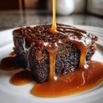 Close-up of a square of sticky toffee pudding recipe being drenched in rich, flowing toffee sauce.