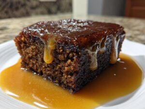 A close-up of a rich, dark slice of sticky toffee pudding recipe covered in dripping toffee sauce.
