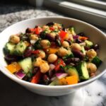 Close-up of a vibrant bean salad featuring chickpeas, kidney beans, cucumber, and peppers in a white bowl.