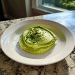 A mound of bright green, creamy cilantro lime sauce garnished with fresh herbs on a white plate.