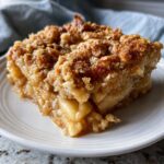 A close-up shot of a square serving of warm apple crisp recipe with a thick, buttery oat topping.