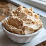 A close-up of fluffy, whipped cinnamon butter piled high in a small white serving bowl.